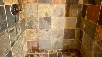 A shower with a tiled wall and floor, a handheld showerhead, and a bottle of shampoo on the wall.
