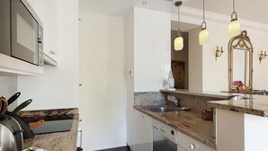 A modern kitchen with a granite countertop, stainless steel appliances, and pendant lighting. - Romantic 2 Bed with Peekaboo Eiffel View in Foodie Heaven (Paris)