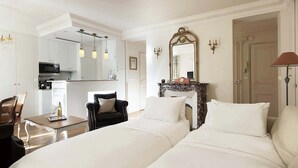A hotel room with two beds, a dining table, a chair, a kitchen area, and a mirror. - Romantic 2 Bed with Peekaboo Eiffel View in Foodie Heaven (Paris)
