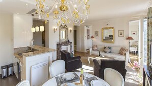 A spacious living area with a chandelier, a fireplace, a dining table set for four, and a sofa. - Romantic 2 Bed with Peekaboo Eiffel View in Foodie Heaven (Paris)