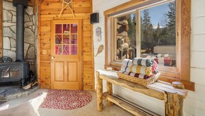 L’intérieur d’un chalet en bois est doté d’une cheminée en pierre, d’un banc en bois sur lequel est posé un panier rempli de serviettes, et d’une grande fenêtre offrant une vue sur l’extérieur.