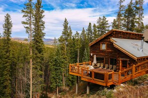 A log cabin with a deck, surrounded by tall pine trees and mountains in the background. - Cabin in the Woods! PET Friendly, Private Outdoor Hot Tub, Gas Grill, Secluded (Breckenridge)