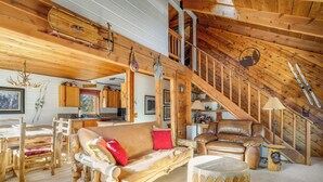 L’intérieur d’un chalet rustique, avec un escalier en bois, un canapé en cuir, une table à manger et un coin cuisine.