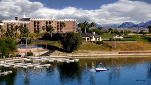 Un hotel con un edificio grande, un muelle con barcos y montañas al fondo.