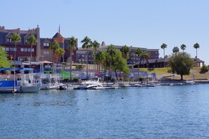 A marina with several boats docked, a building with a distinctive tower, and palm trees in the background.