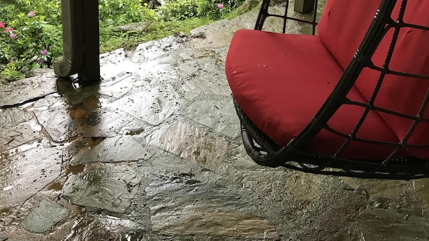 Punaisella pehmusteella varustettu riipputuoli katetulla alueella, josta avautuu näkymä metsäiseen puroon.