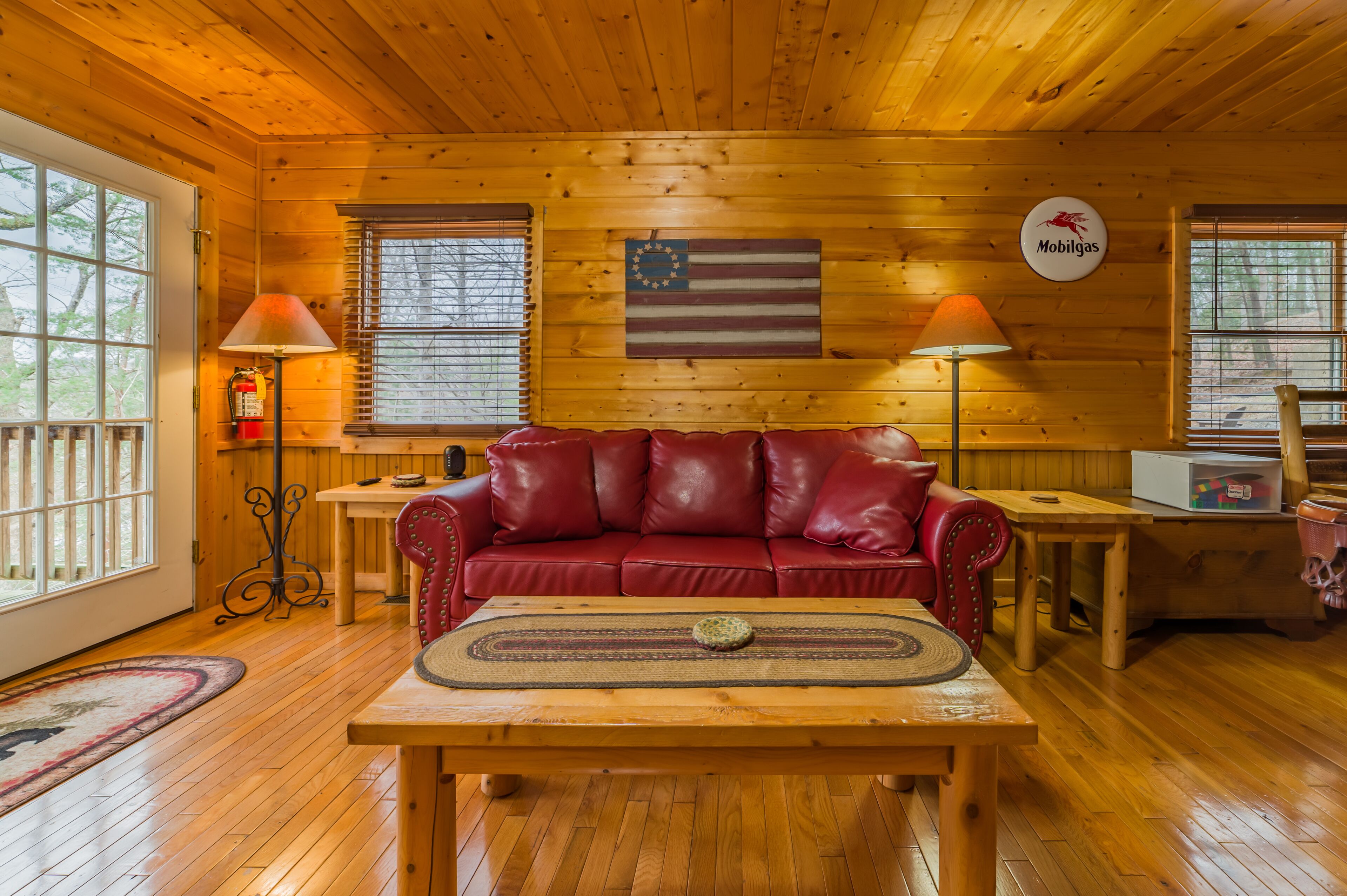 L’intérieur d’un chalet accueillant, avec un plancher en bois, un canapé en cuir rouge, une table basse en bois et deux lampes.
