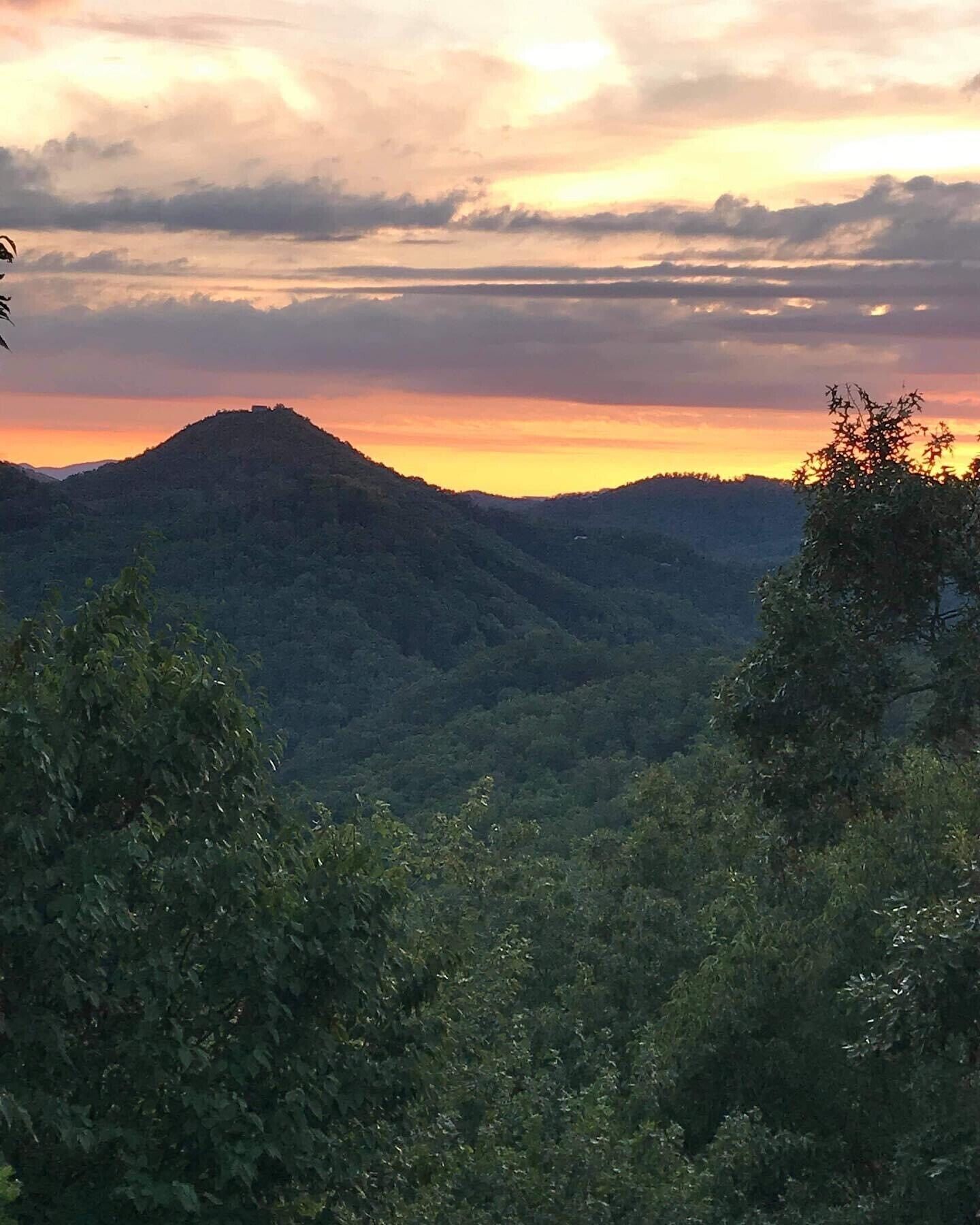 A mountainous landscape with dense forest in the foreground and a hill with a structure on top.