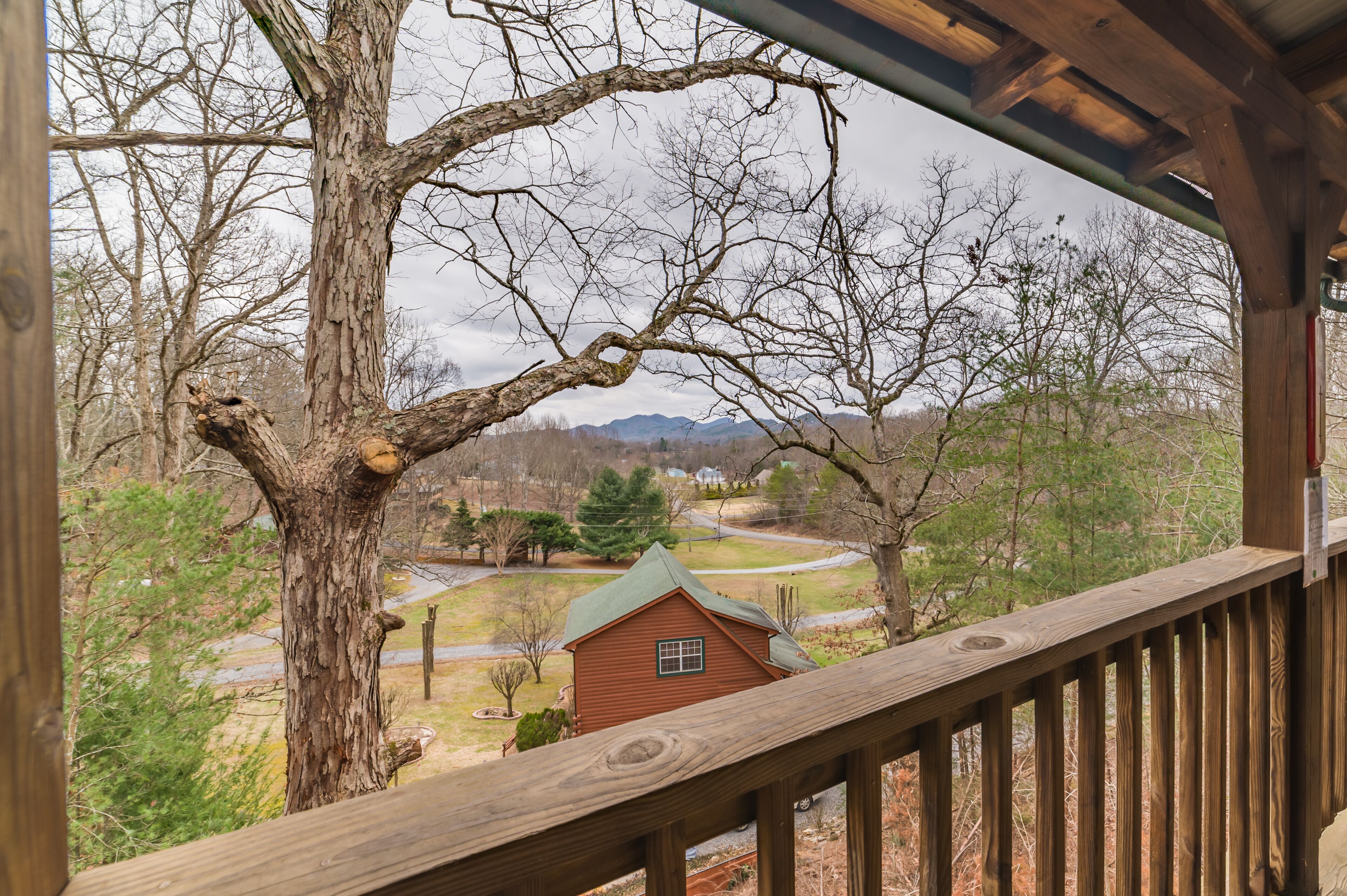 A wooden deck overlooking a rural landscape with a small house and a large tree.