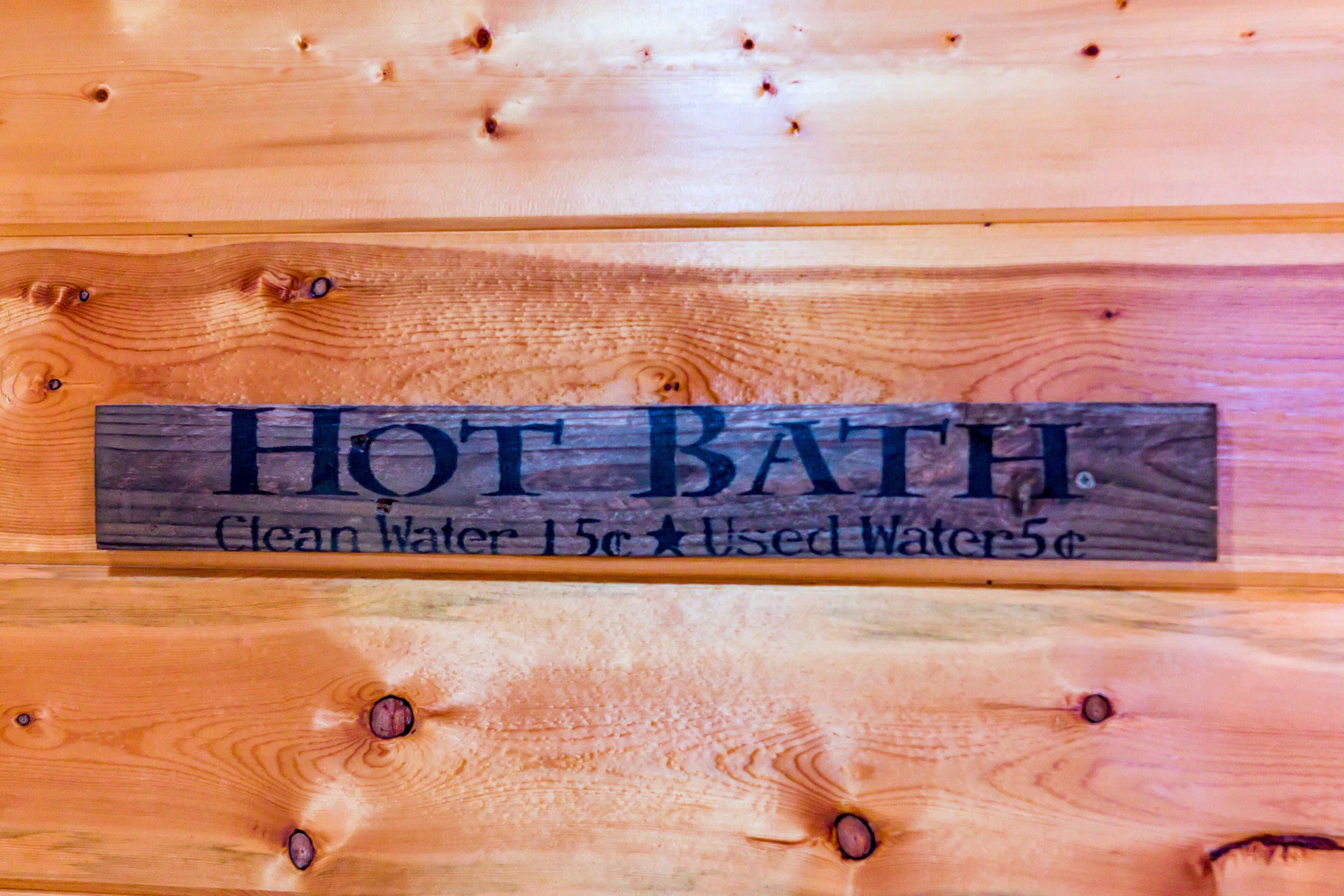 A wooden sign with the text "HOT BATH" and pricing information for clean and used water.