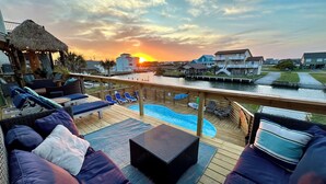 Una terraza con sillones de descanso y piscina, con vistas al frente marítimo y casas al fondo.
