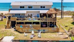 Una casa frente al mar de dos pisos, con un porche, piscina y una estructura de techo de paja.