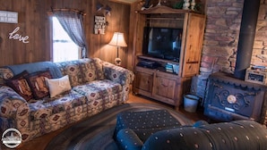 Una sala de estar acogedora con un sofá estampado, un televisor, una chimenea de piedra y paredes de madera.
