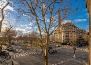 A city street with a large building in the background, trees lining the road, and vehicles on the road.