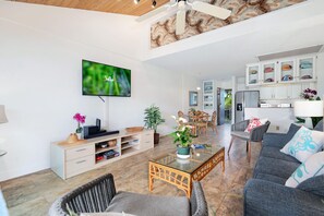 Uma sala de estar moderna com televisão de tela plana, área de jantar com cadeiras, cozinha com armários e ventilador de teto.