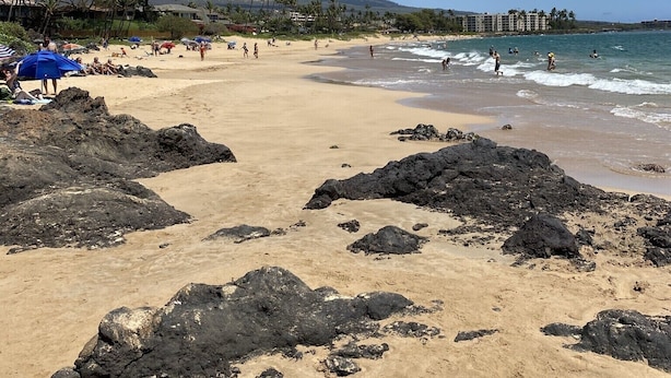 Una playa con zonas rocosas, gente tomando el sol y un cielo despejado.