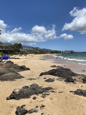 Une plage avec des zones rocheuses, des gens qui prennent un bain de soleil et un ciel dégagé.