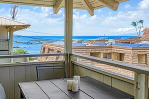 Een balkon met een tafel en stoelen, met uitzicht op een strand met zonnepanelen op gebouwen en een heldere lucht.