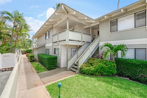 A two-story residential building with a covered front porch, a staircase, and a well-maintained lawn.