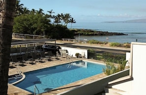 A pool area with lounge chairs and a view of the ocean.