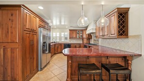 A kitchen with wooden cabinets, a stainless steel refrigerator, a marble countertop, and two bar stools. - WALK to Beach, Pier and Downtown - Parking - BBQ - View (Pismo Beach)
