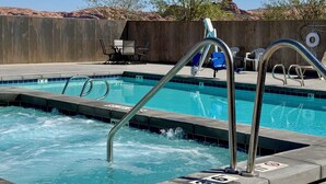 Ein Swimmingpool mit Treppen und Liegestühlen, umgeben von einem Holzzaun und einer Wüstenlandschaft.