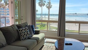A living room with a sofa, a coffee table, and a large window offering a view of a beach and pier. - PRICE REDUCTION! BEACH FRONT CONDO! 
San Diego-Imperial Beach-Coronado (Imperial Beach)
