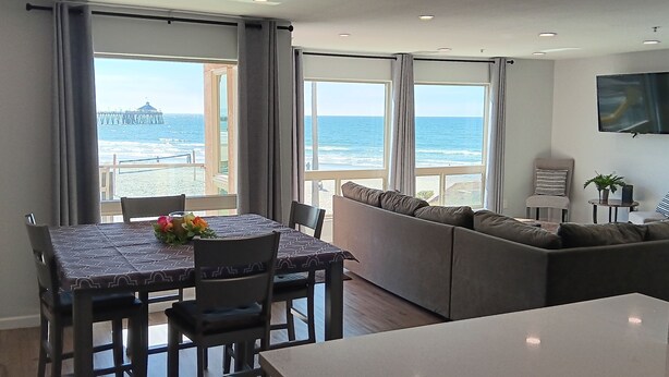 A modern living room with a large window overlooking the ocean, a sofa, a dining table with chairs, and a flat-screen TV mounted on the wall. - PRICE REDUCTION! BEACH FRONT CONDO! 
San Diego-Imperial Beach-Coronado (Imperial Beach)
