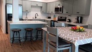 A modern kitchen with grey cabinets, a white countertop, a built-in microwave, a stove, and a sink. There are three stools and a table with a patterned tablecloth. - PRICE REDUCTION! BEACH FRONT CONDO! 
San Diego-Imperial Beach-Coronado (Imperial Beach)
