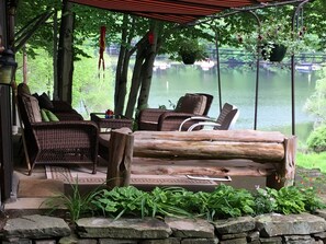 A covered outdoor seating area with wicker furniture and a log bench, overlooking a calm lake. - 4 BR, 2 BA,WIFI,FIREPIT, FIREPLACE, GAS GRILL, SMART TV,BOAT SLIP,POOL, SLPS 9. (Lake Ariel)