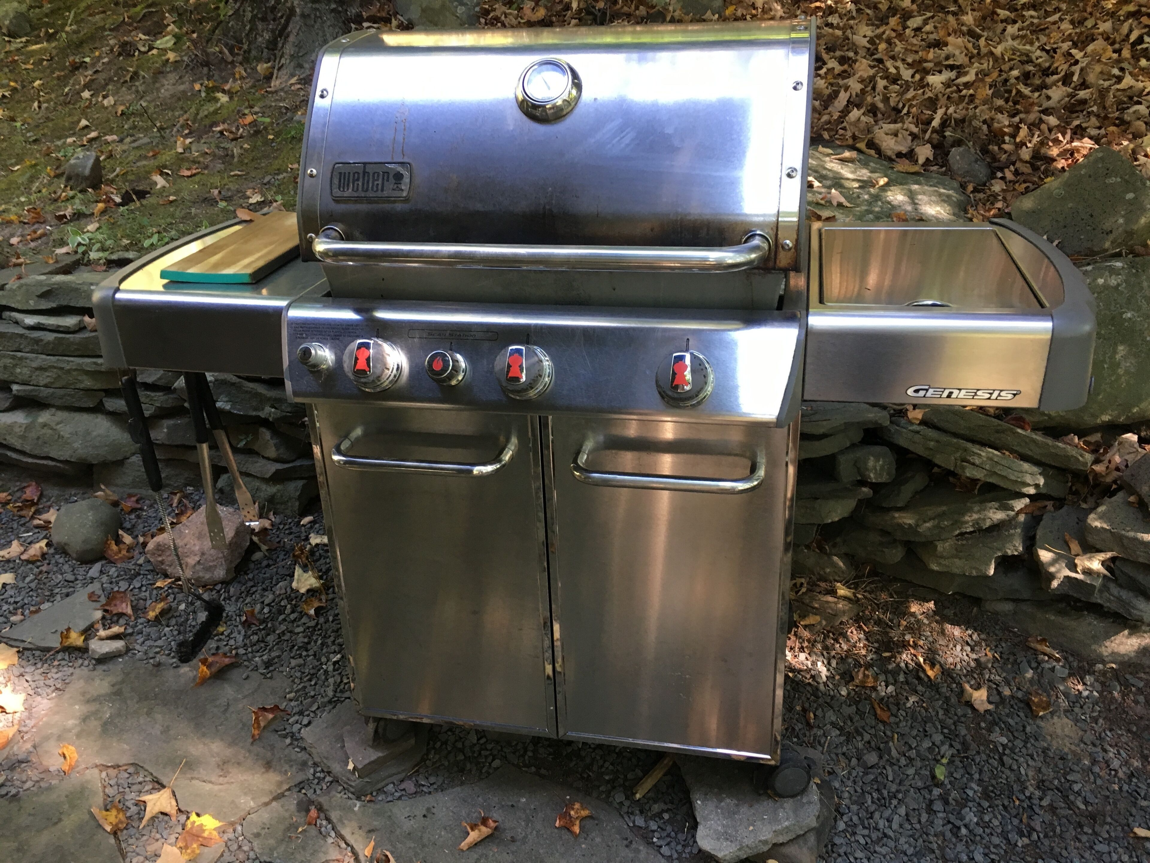 A stainless steel Weber Genesis grill with four burners, a side shelf, and a built-in sink.