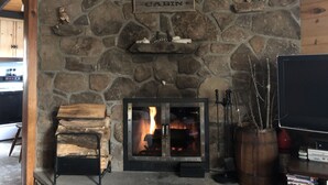 Una llar de pedra amb un rètol que diu "Welcome to Cabin", una televisió sobre un suport a la dreta, i una zona de fusta per emmagatzemar llenya al davant de la llar.