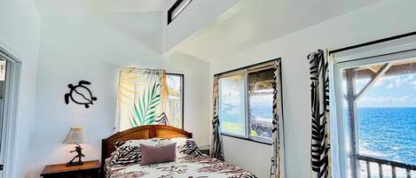 Una camera da letto con un letto, una ventola a soffitto, una finestra vista oceano, un comodino e una lampada.