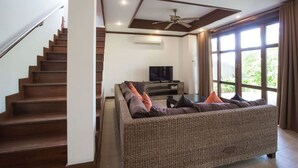 A modern living room with a staircase, a flat-screen TV, and a large window with curtains. - 3 Bedroom Villa TG25 Beach Front Resort SDV282-By Samui Dream Villas (Koh Samui)
