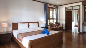 A neatly made bed with a wooden headboard, a nightstand with a lamp, and a chair near a window with curtains. - 3 Bedroom Villa TG25 Beach Front Resort SDV282-By Samui Dream Villas (Koh Samui)