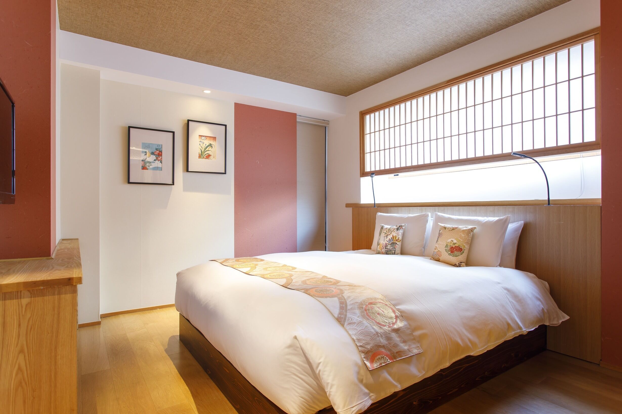 Ein Schlafzimmer mit einem Bett, einem Holztisch, einem Fenster mit Jalousien und zwei gerahmten Bildern an der Wand.