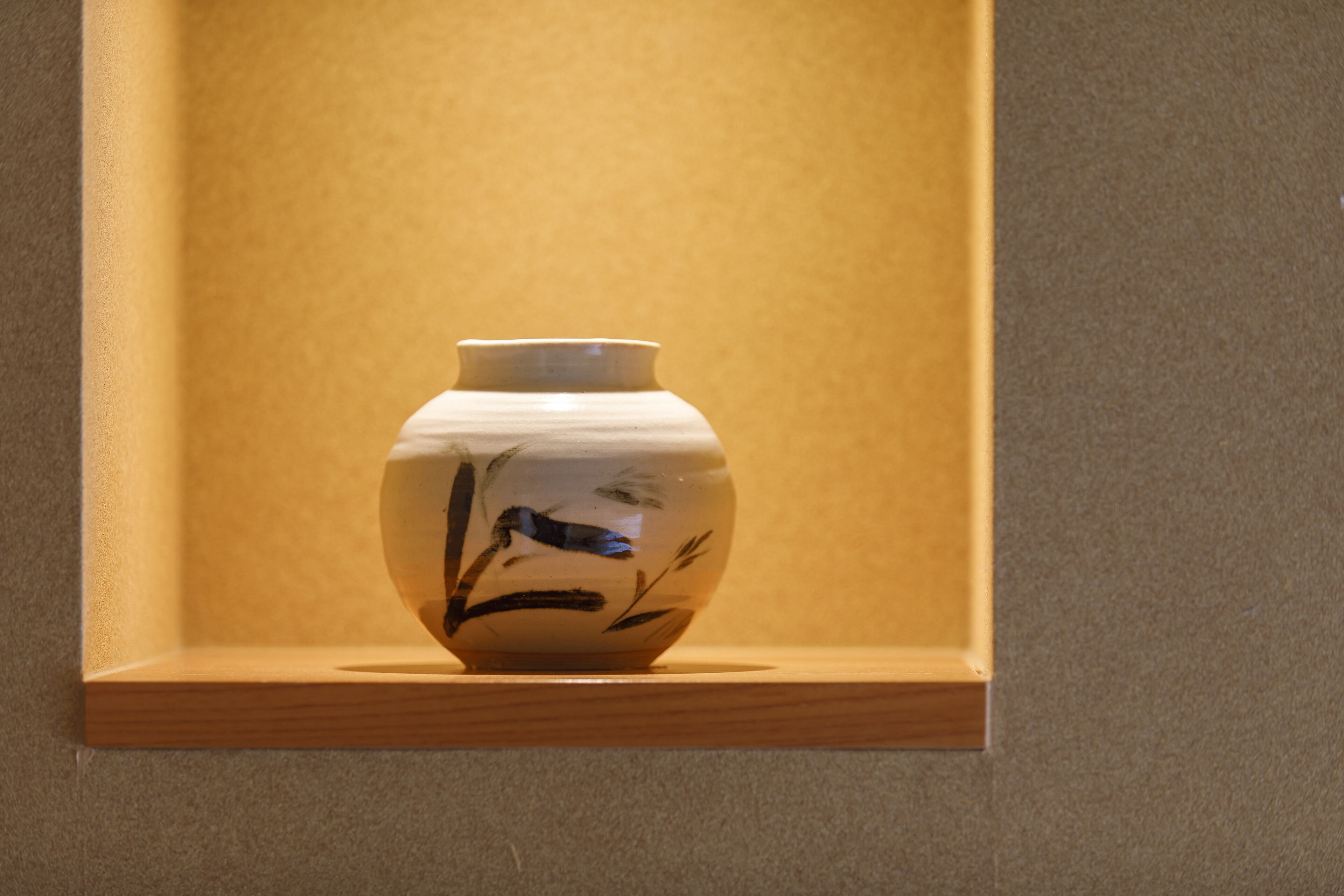 A ceramic vase with floral designs on a wooden shelf against a textured wall.