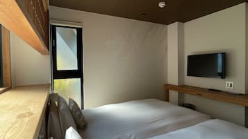 A bedroom with a bed, a TV on a wooden stand, and a window with blinds.