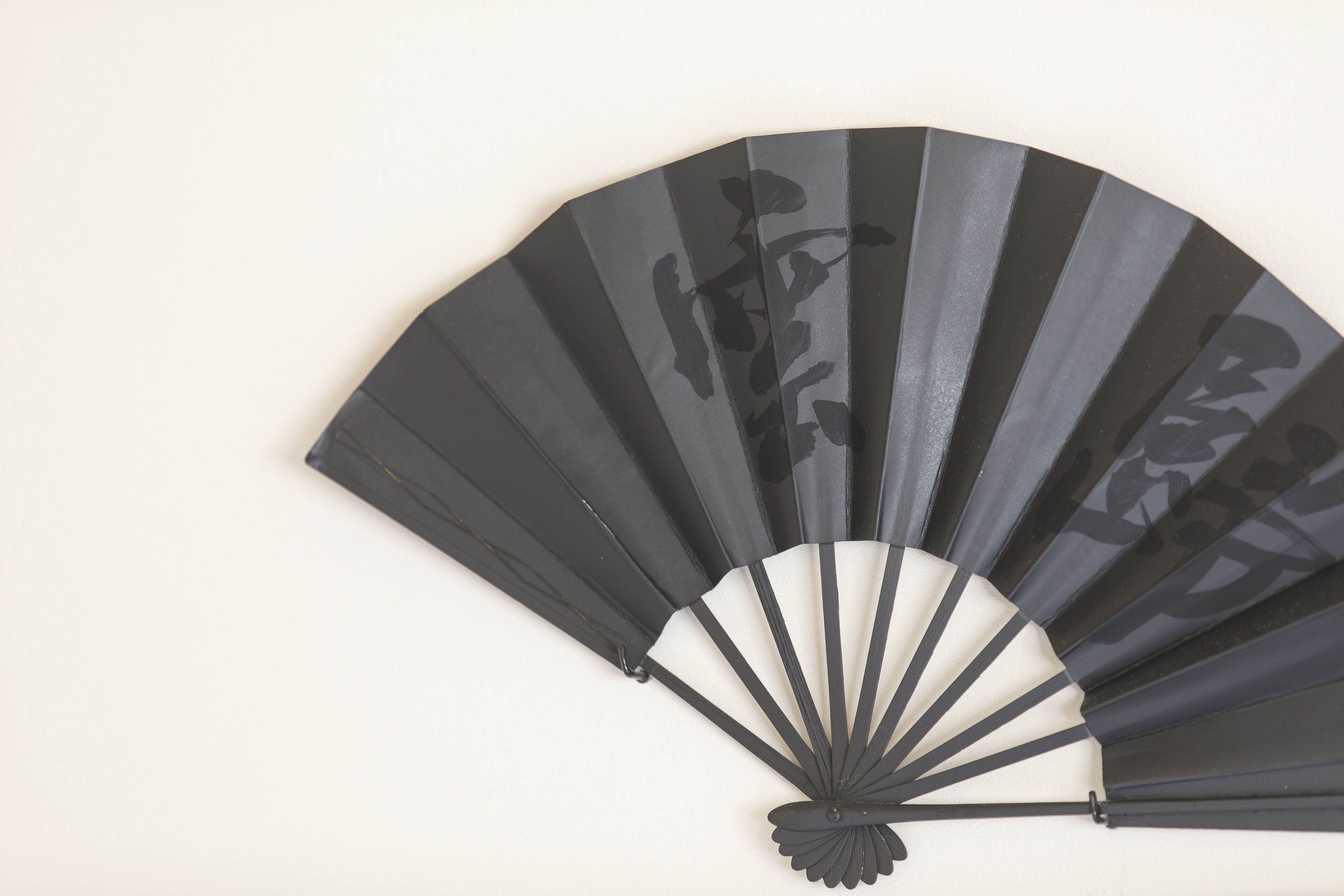 A black fan with a traditional design against a plain background.