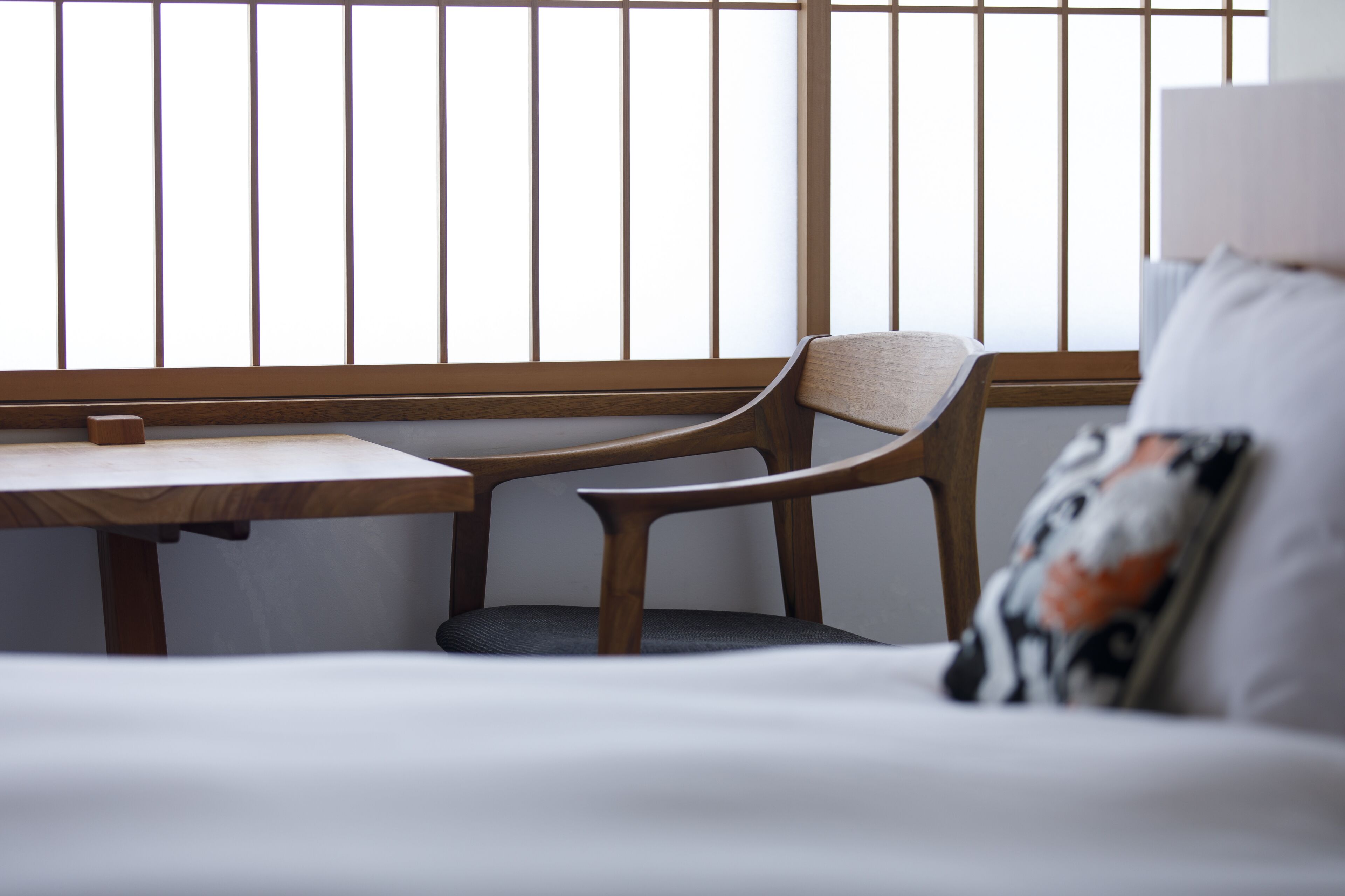 A room with a wooden table, a chair, and a bed with a pillow.