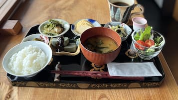 A tray with various dishes including rice, soup, and salad, placed on a wooden table.