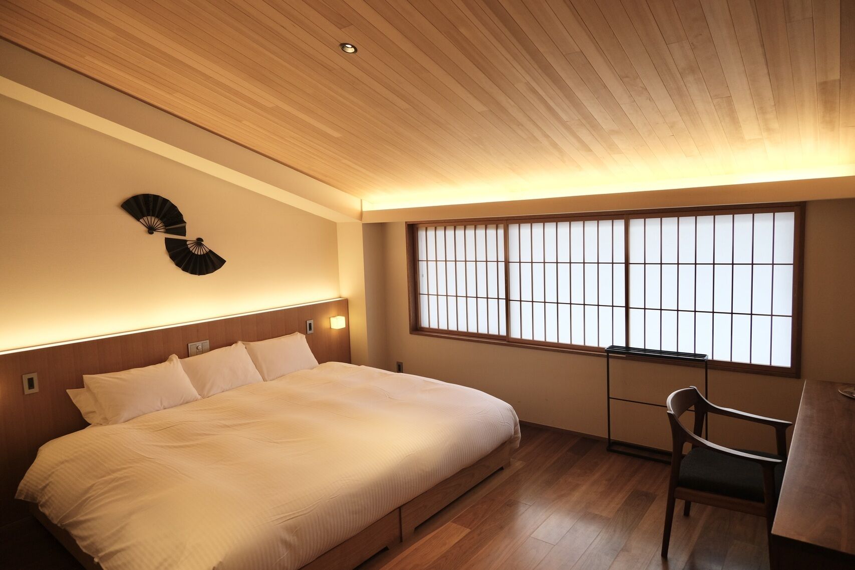 Ein Hotelzimmer mit Bett, Stuhl, Tisch, Ventilator und einem Fenster mit Blick.