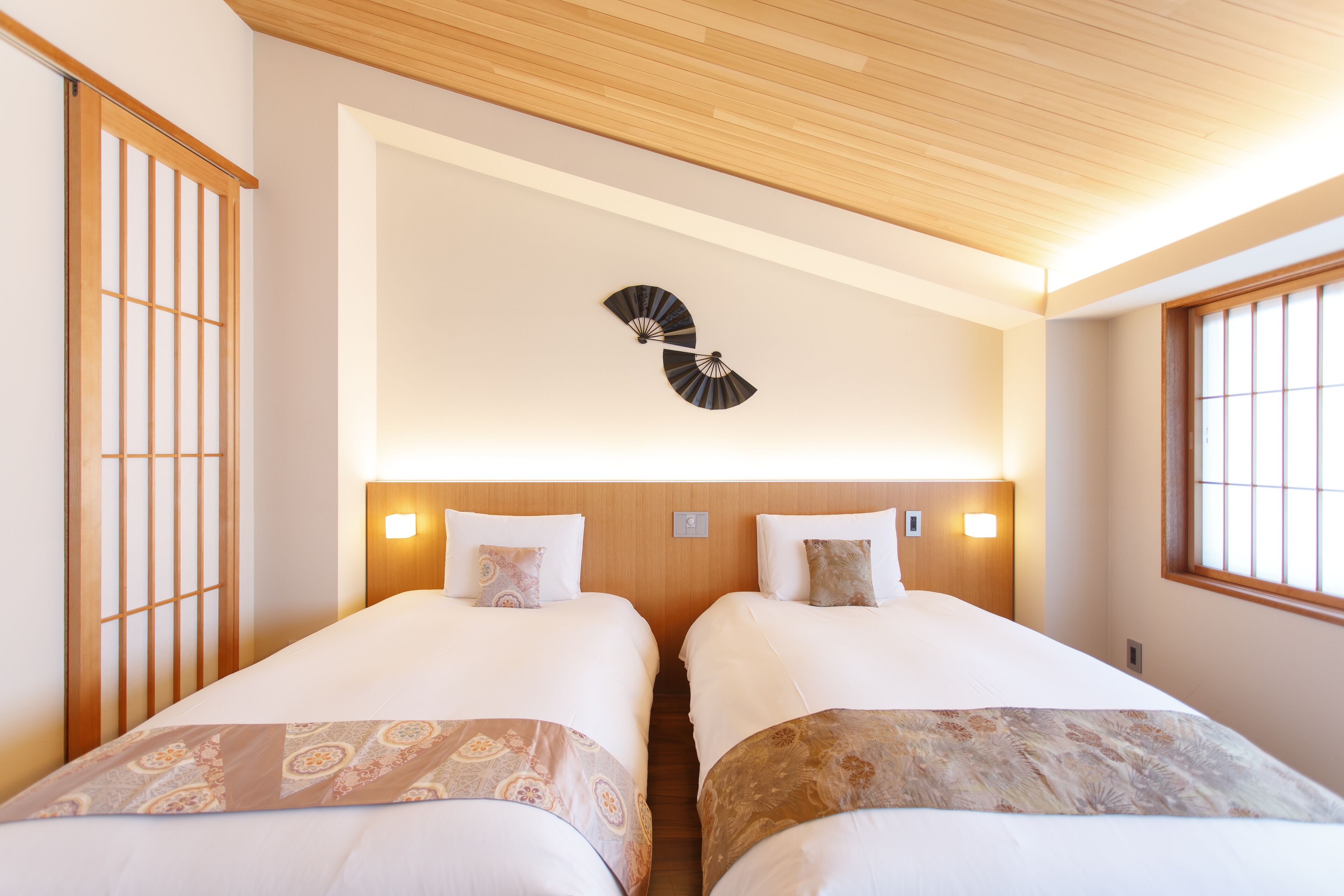 A hotel room with two beds, a wooden ceiling, and a wall-mounted fan.