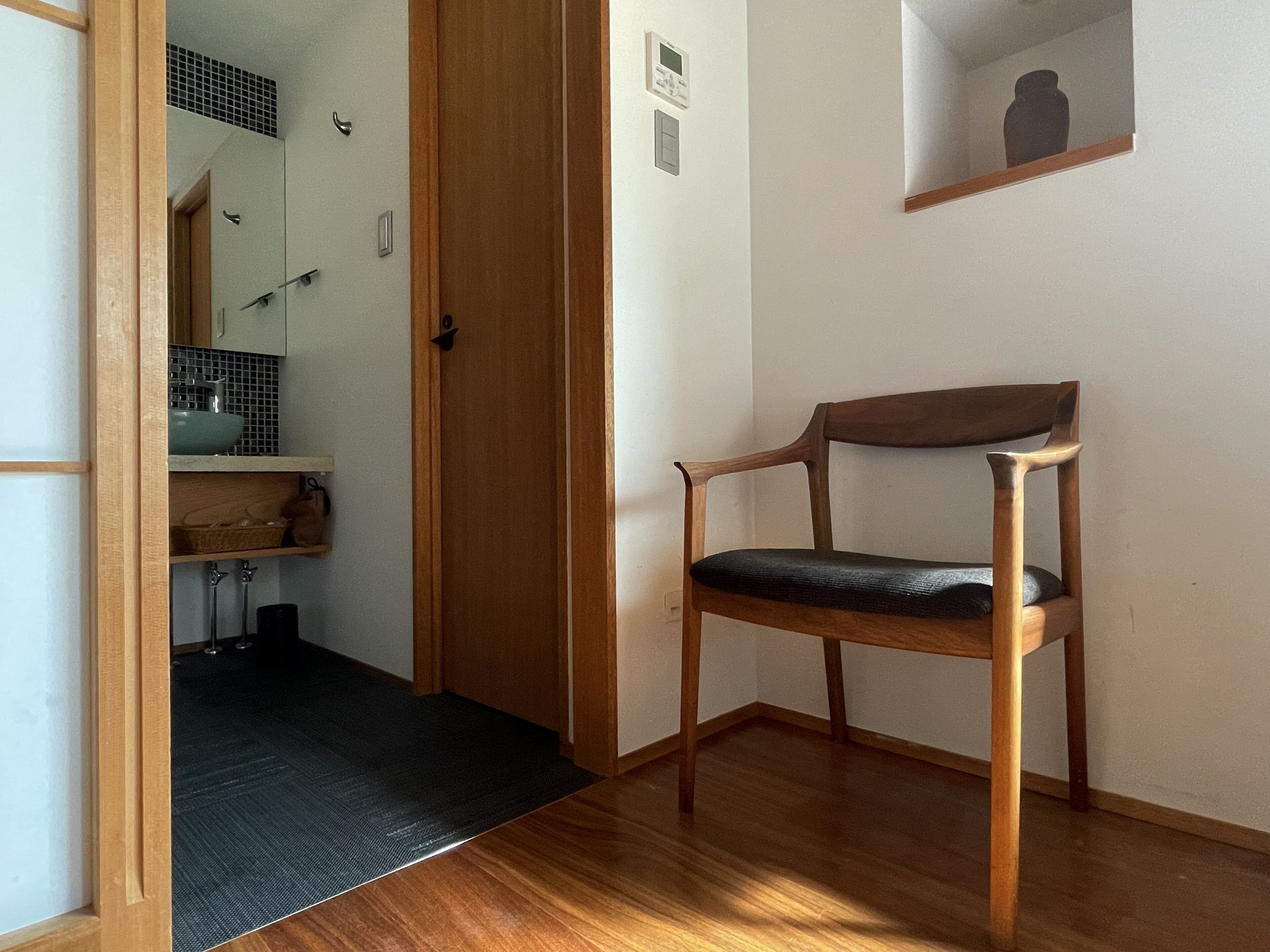 A wooden chair in a hallway with a door leading to a bathroom.