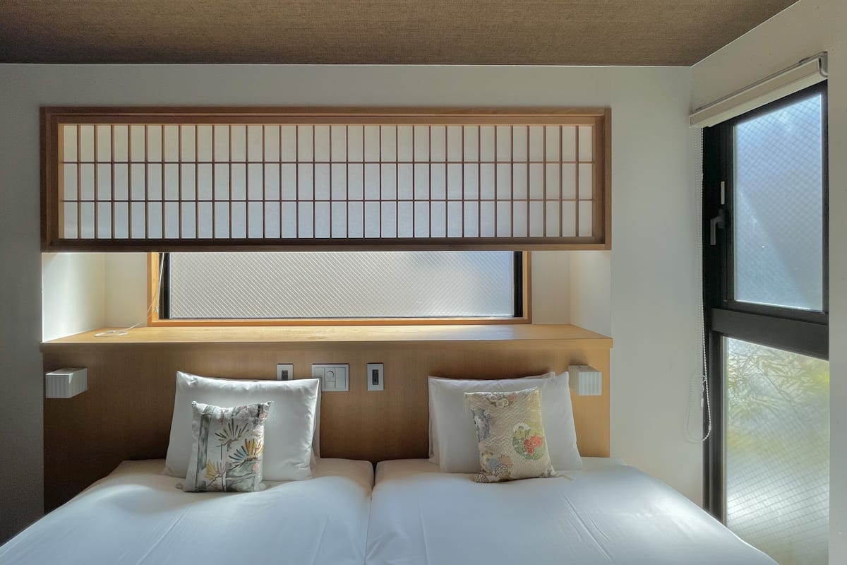 Hotellihuone, jossa on sänky, ikkunasta avautuva näkymä ja puinen pääty.