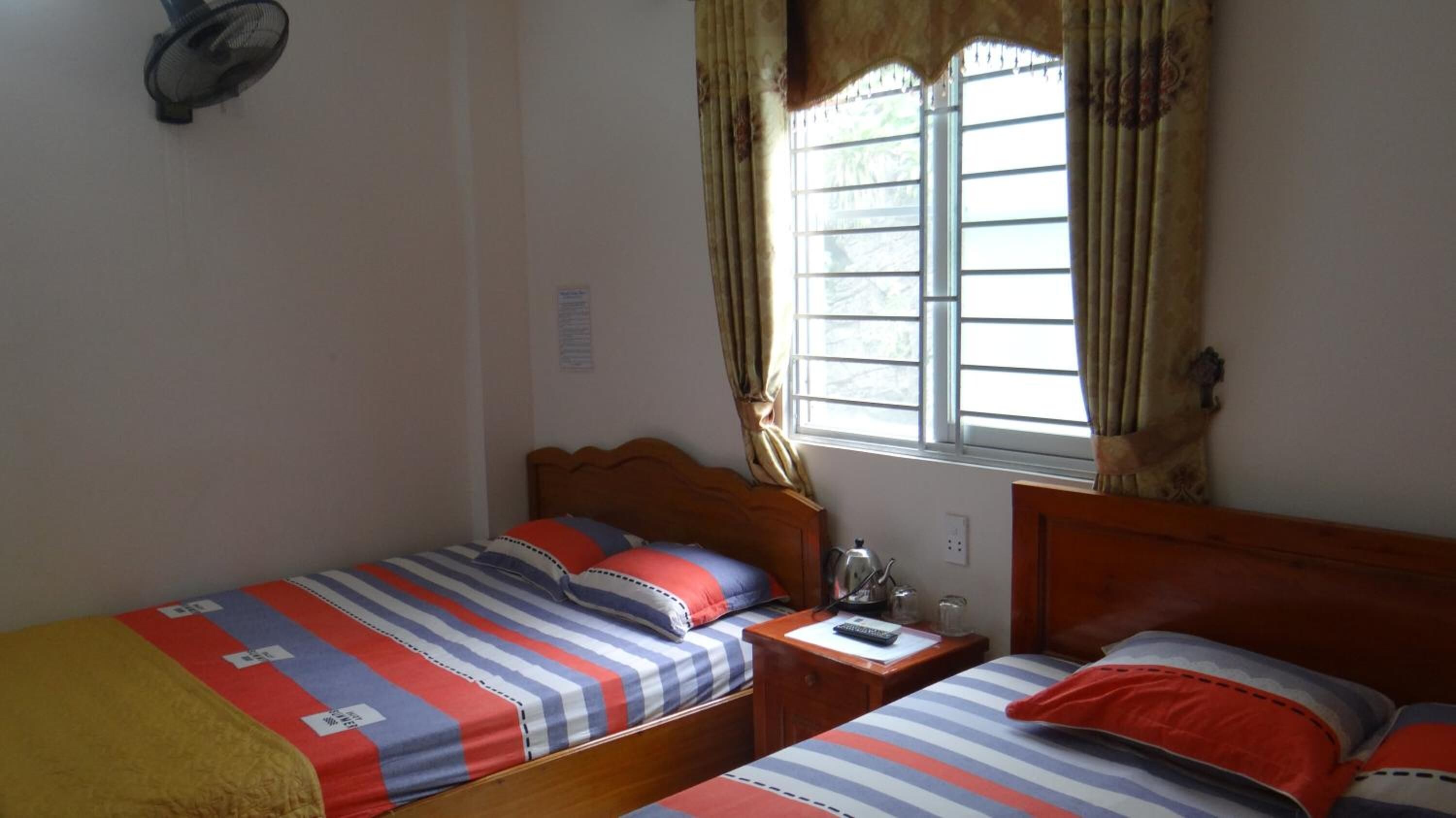 A room with two single beds, a wooden nightstand, a small table, and a window with curtains.