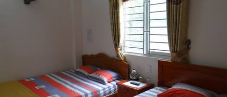 A room with two single beds, a wooden nightstand, a small table, and a window with curtains.