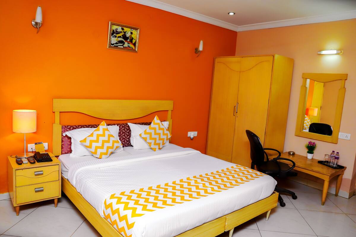 Quarto de hotel com uma cama grande, uma escrivaninha, uma cadeira, um guarda-roupa e uma mesa de cabeceira com abajur.