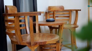 A wooden chair and table set against a white wall, with a small black object on the table. - Akatara Stay Jimbaran (Jimbaran)