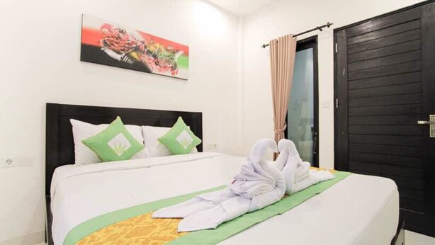 A hotel room with a neatly made bed, a painting on the wall, and a door with a curtain. - Akatara Stay Jimbaran (Jimbaran)